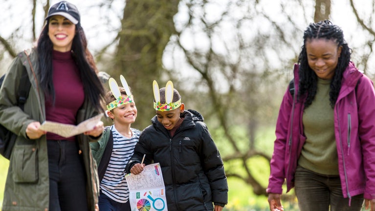 Teulu yn mwynhau helfa Basg drwy'r goedwig mewn un o safleoedd yr Ymddiriedolaeth Genedlaethol